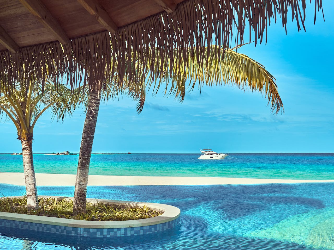 Scenic tropical beach with swaying palms, turquoise water, and a yacht.